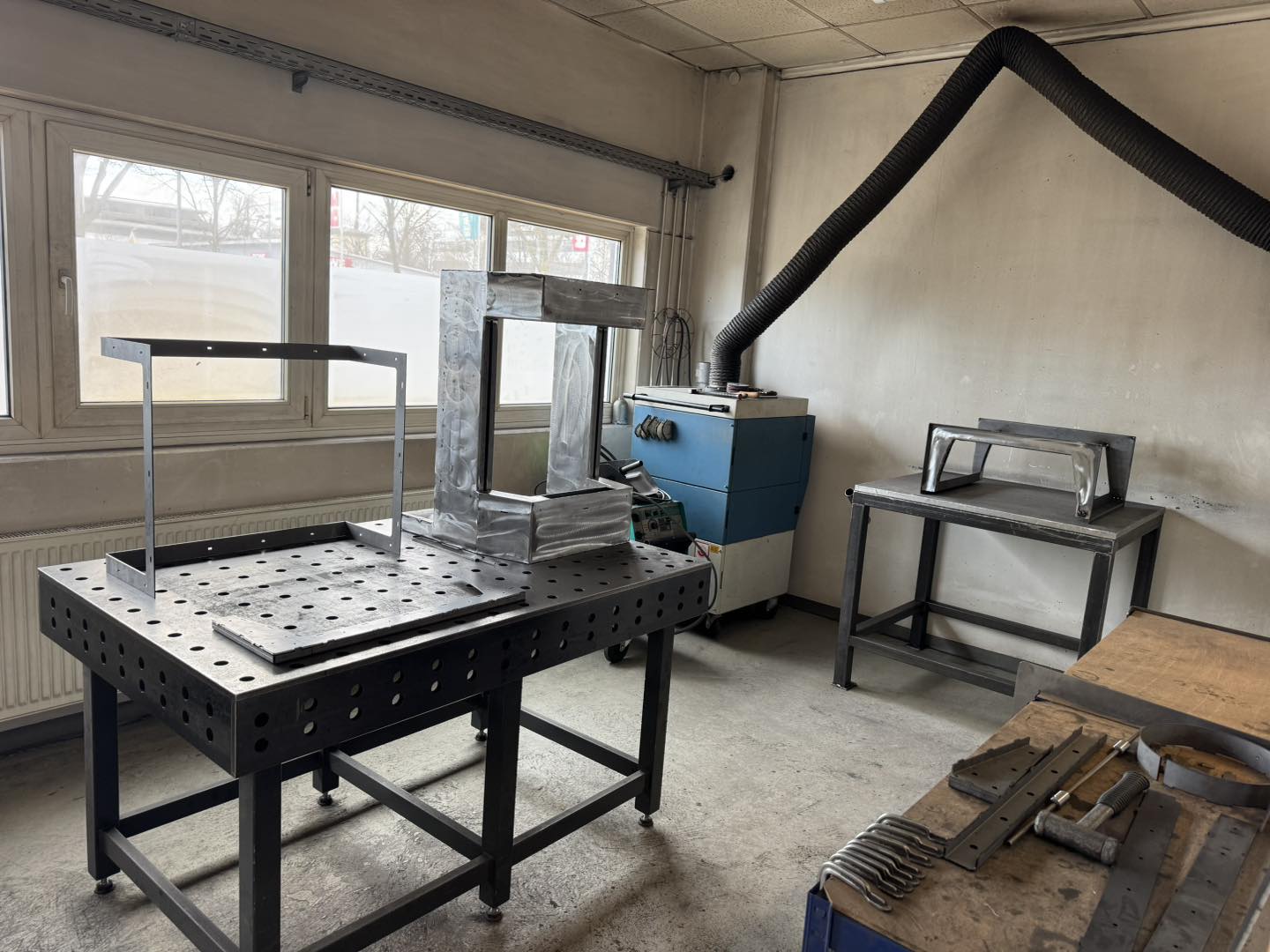 Ein rohes Stahlgehäuse wird auf einem professionellen Schweißtisch in der AMBIO Werkstatt in Dorfen bearbeitet. Im Hintergrund ist eine Absauganlage sichtbar.